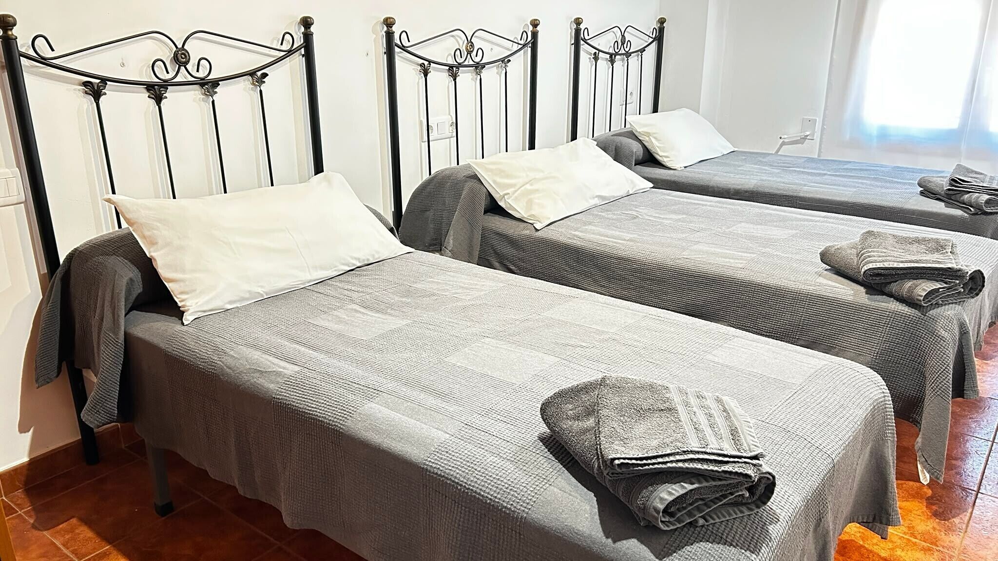 Ein Hotelzimmer mit zwei Einzelbetten, jeweils mit einer grauen Tagesdecke und einem weißen Kopfkissen.