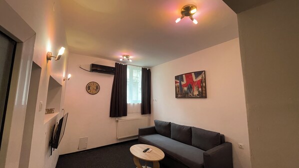 A living room with a gray sofa, a small round table, a clock, and a painting on the wall.