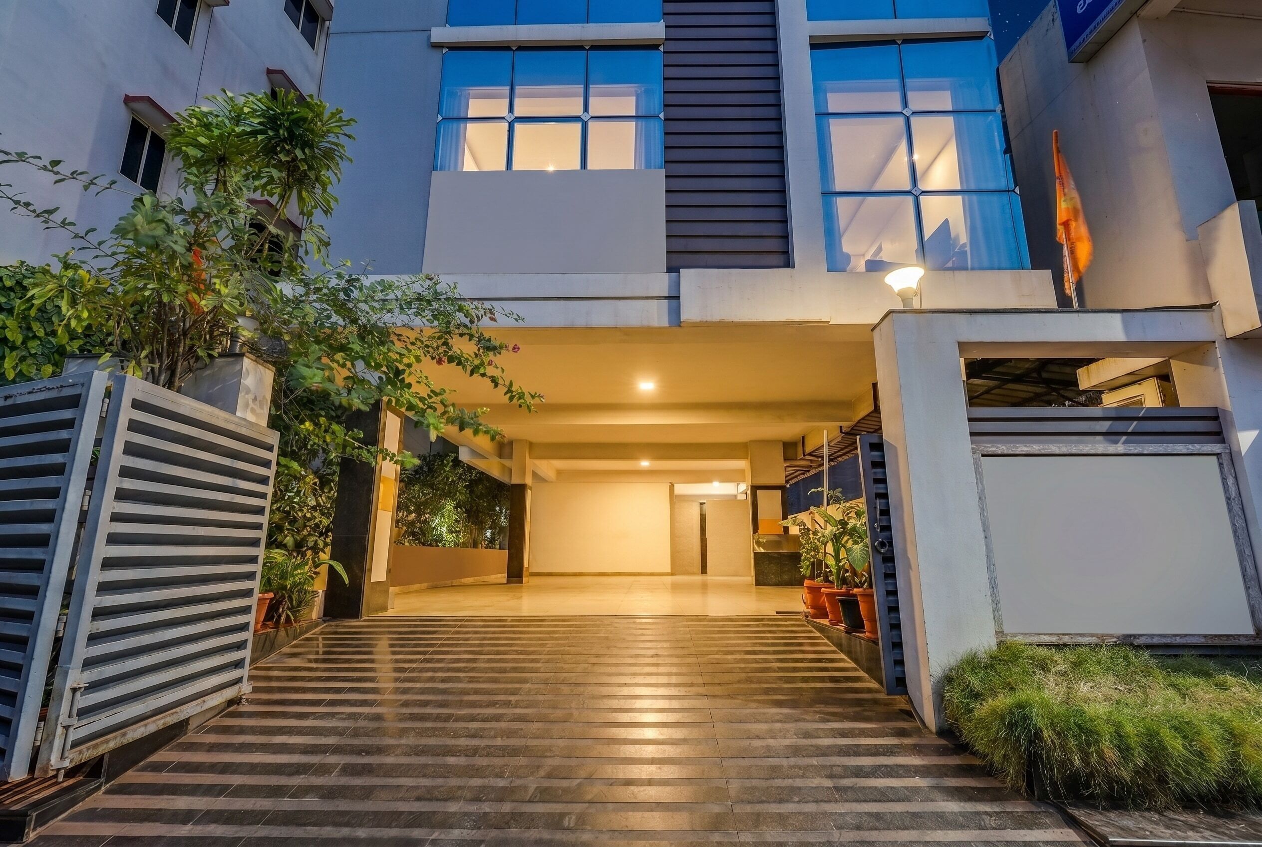 A modern building entrance with a covered walkway, potted plants, and a clear sky.
