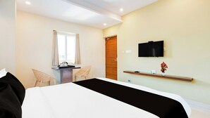 Una habitación de hotel con una cama, un escritorio, una silla, un televisor y un estante pequeño con un florero.