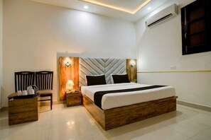 Quarto de hotel moderno com uma cama grande, mesa de cabeceira de madeira, uma cadeira e ar condicionado fixado na parede.