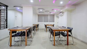 A conference room with multiple tables and chairs, equipped with ceiling lights and an air conditioning unit. - Collection O Atchutapuram (Visakhapatnam)