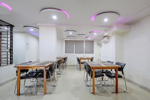 A conference room with multiple tables and chairs, equipped with ceiling lights and an air conditioning unit.