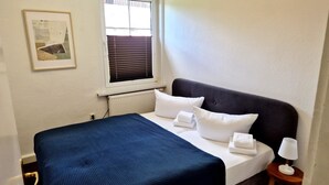 Habitació d'hotel amb llit, finestra amb persianes, radiador i un quadre al mur.