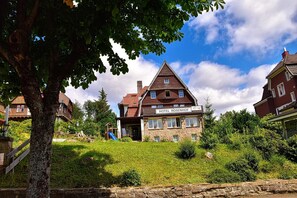 Perinteinen rakennus, jonka yläpuolella on kyltti, jossa lukee »HOTEL ROSENHOF». Se sijaitsee maaseutumaisemassa, jossa on kivimuuri, vehreää kasvillisuutta ja kirkas taivas.