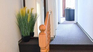 Una escala amb barana de fusta que condueix a una plataforma. Hi ha una planta en test a la plataforma, i una finestra amb cortines es veu al fons.