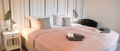 Un dormitorio ordenado con una cama, mesitas de noche, una silla y una planta en maceta.