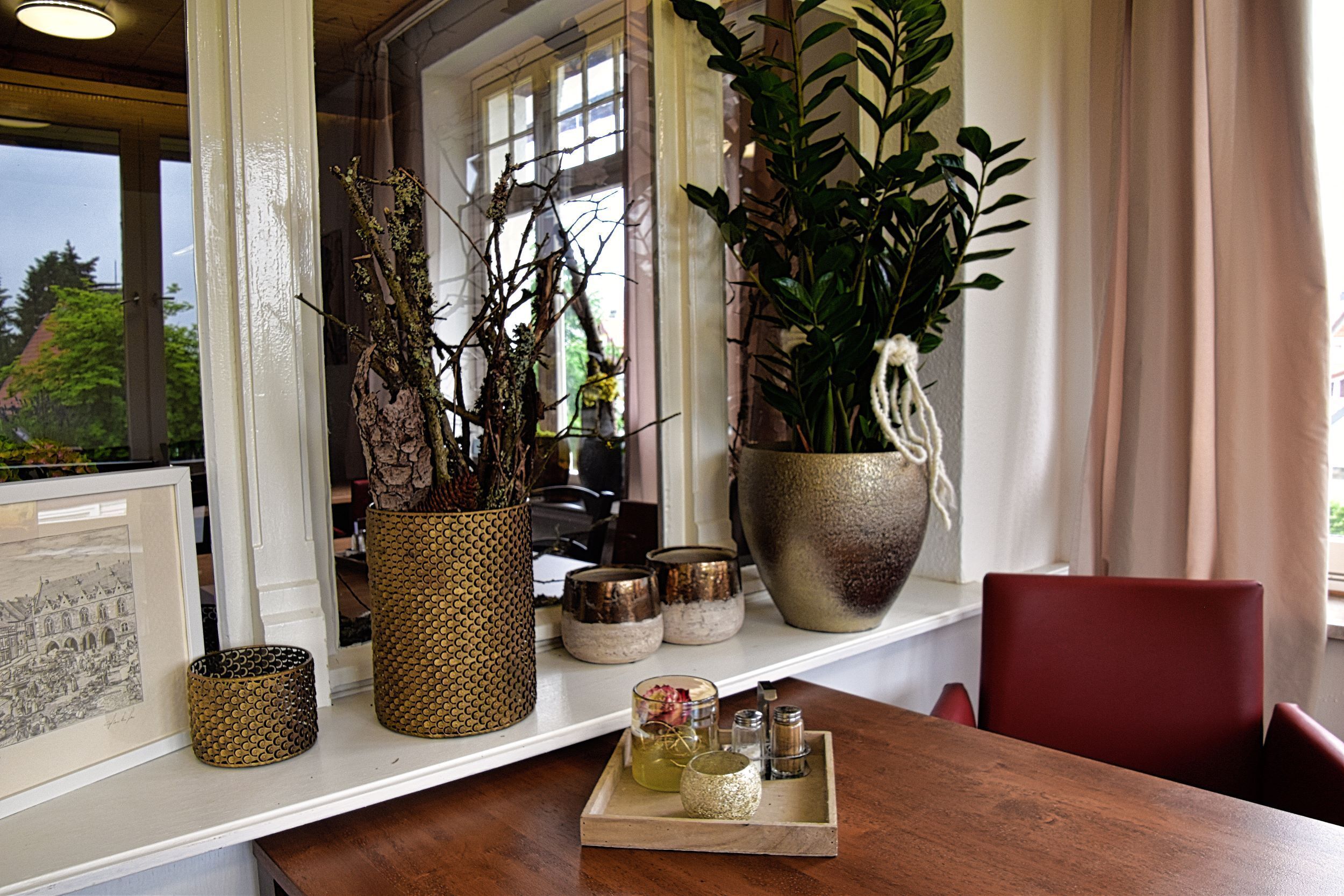 Un comedor con una mesa de madera, una silla roja y una ventana con plantas y un cuadro enmarcado.