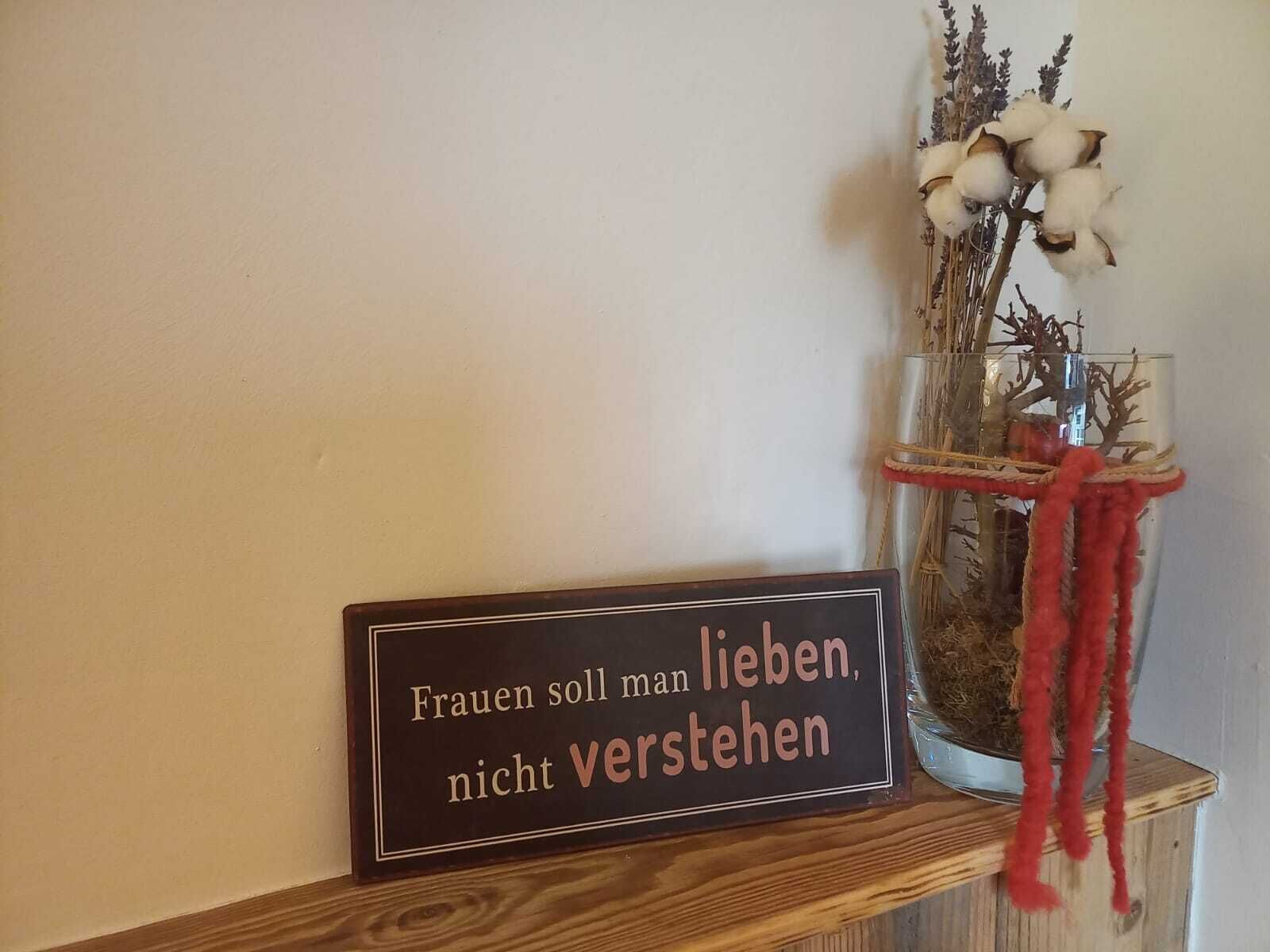 A wooden shelf with a sign and a vase with dried plants.