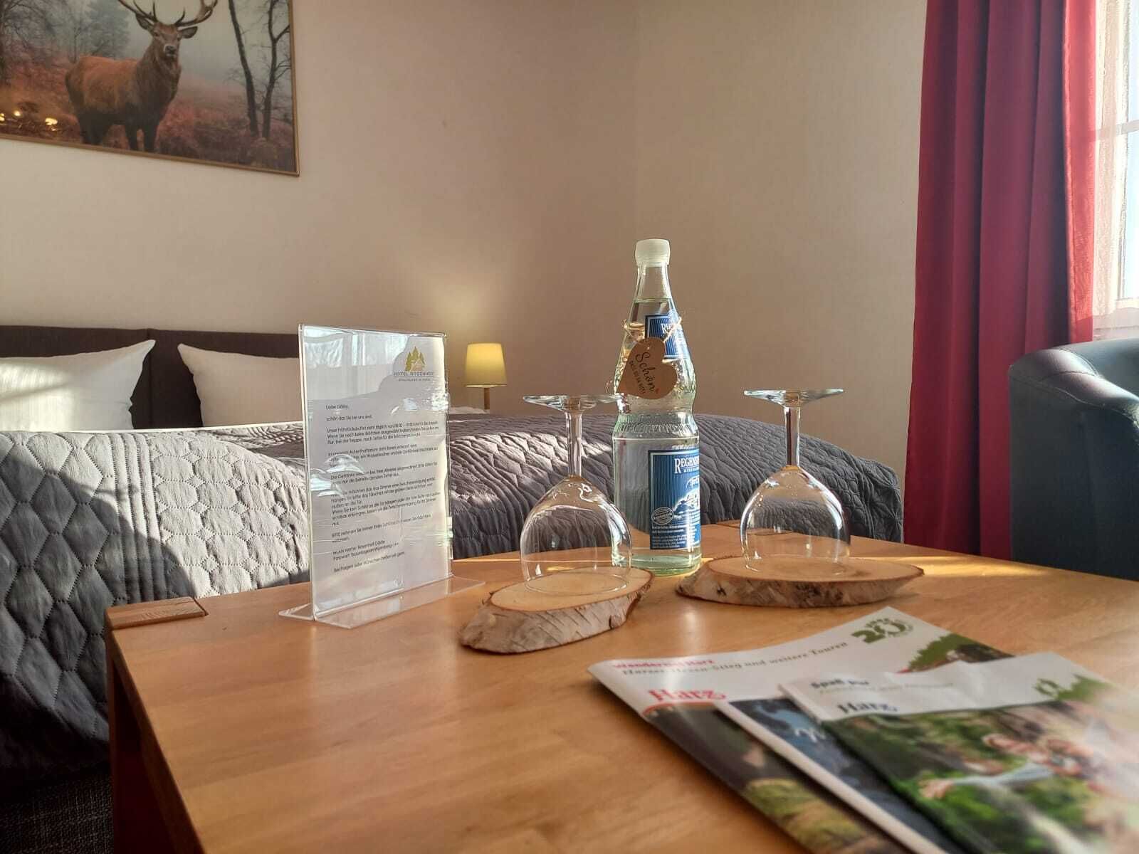 A hotel room with a bed, a wooden table with a menu, a bottle of liquor, and a magazine.