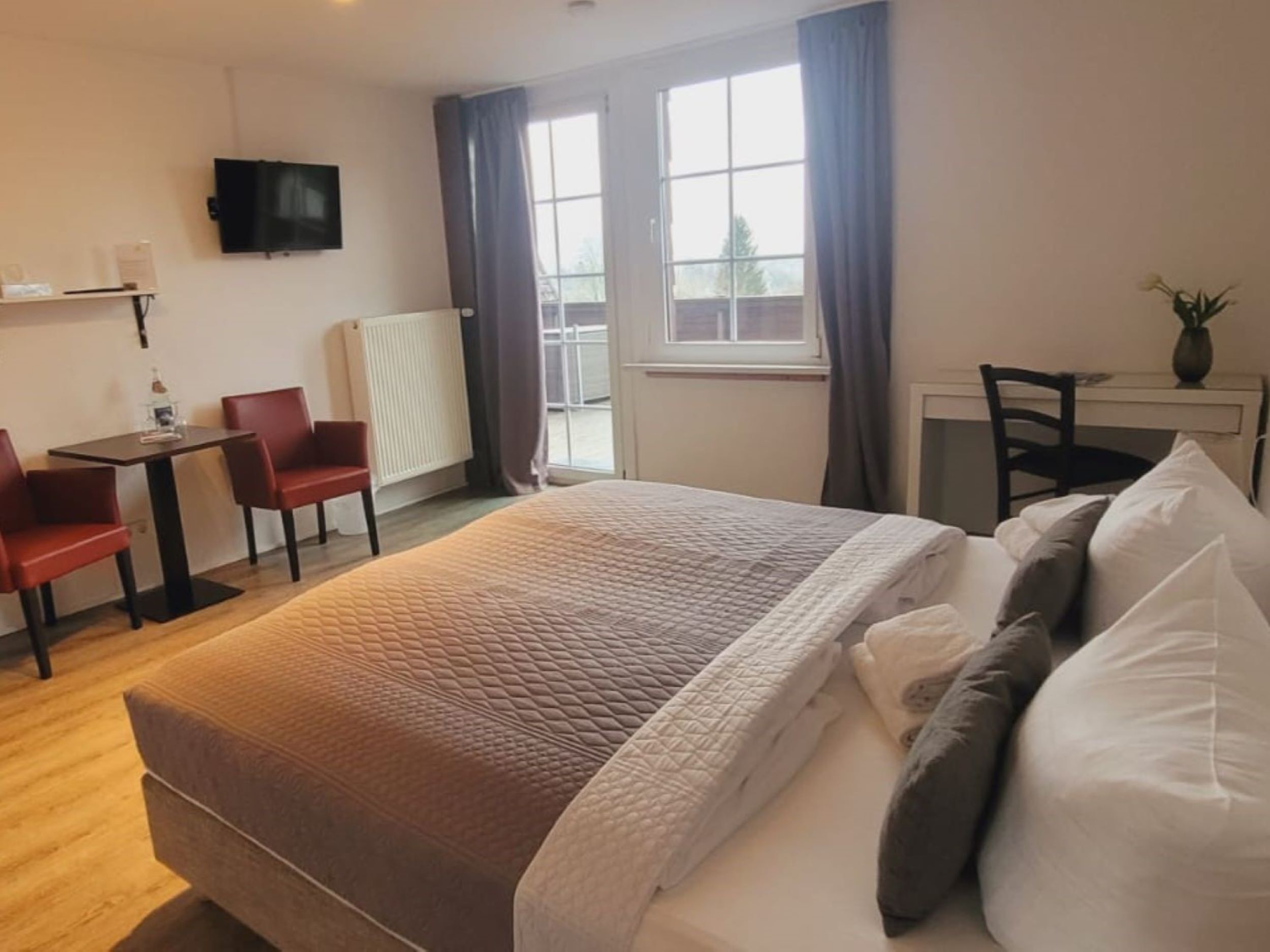 A hotel room with a bed, a desk, two chairs, a television, and a window.