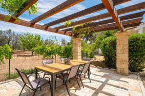 An outdoor patio with a wooden table and chairs, surrounded by stone pillars and a pergola. - Casa Serena: with Pine Forest, Jacuzzi Tub & BBQ near the beach, Pet Friendly (San Vito dei Normanni)