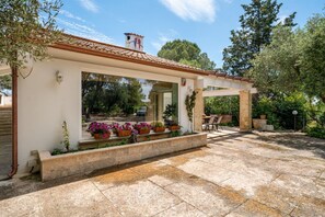 Eine überdachte Terrasse im Freien mit Fliesenboden, Pflanzkübeln und einer Pergola.
