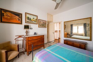 Ein Schlafzimmer mit einem Bett, einem Schminktisch, einem Sessel und einem Deckenventilator.