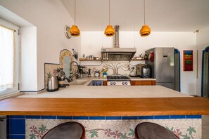Eine Küche mit einer zentralen Kochinsel, Pendelleuchten an der Decke, einem Edelstahlkühlschrank und einer gefliesten Spritzwand.