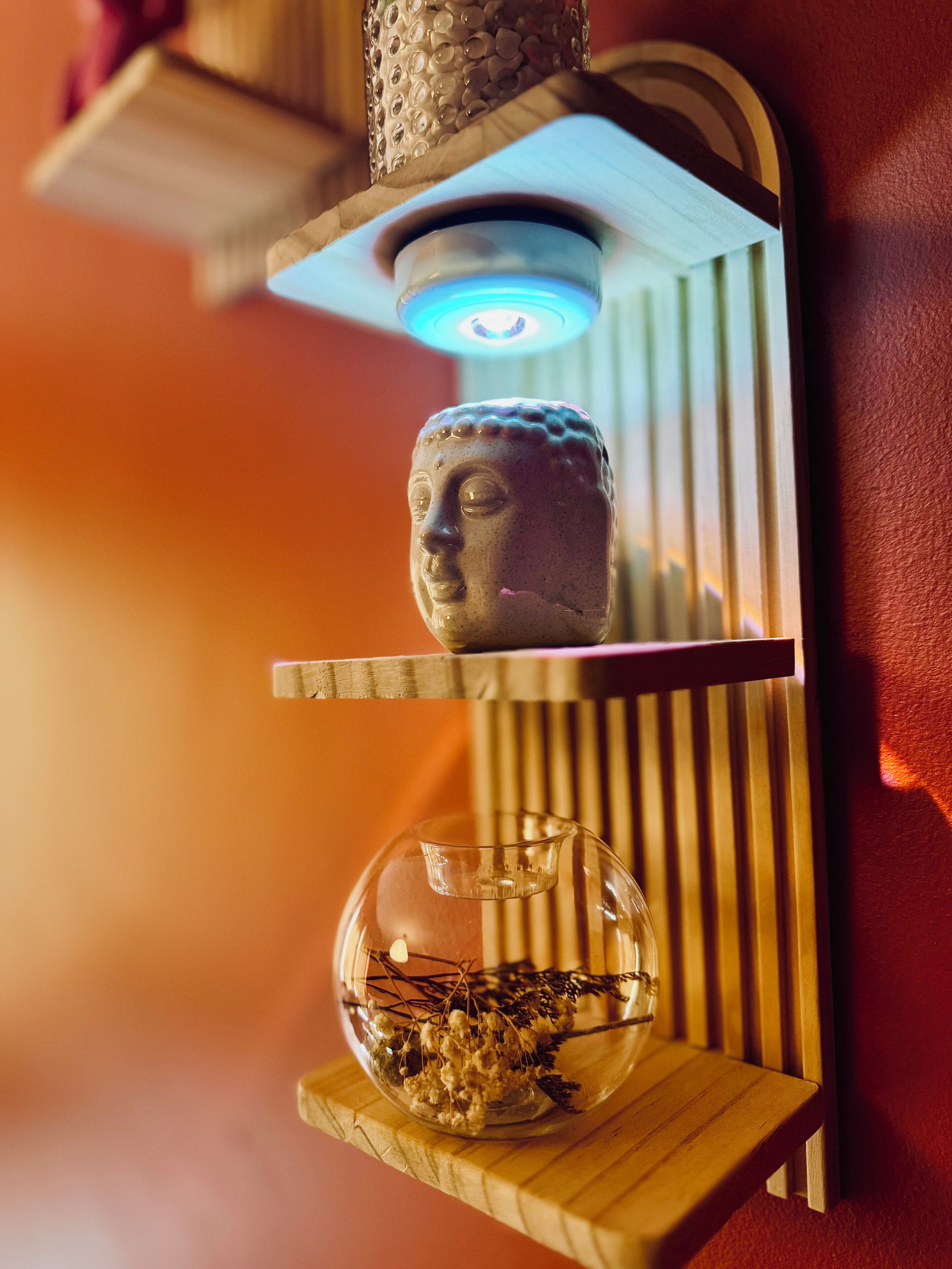 Une étagère murale ornée d’une statue de Bouddha et d’un bol en verre contenant des fleurs séchées.