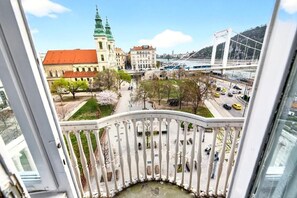 Blick von einem Balkon auf eine Stadtlandschaft mit einem markanten Gebäude mit Gründach, einer weißen Brücke und einem Fluss.