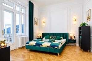 Une chambre avec un grand lit, un radiateur, une fenêtre avec des rideaux, une table de chevet, une armoire et des lampes fixées au mur.