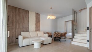 A modern living room with a sofa, a coffee table, wicker chairs, and a staircase. - Sani Astera Deluxe by Rentals Pro - Sani Halkidiki (Sani)