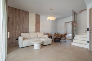 A modern living room with a sofa, a coffee table, wicker chairs, and a staircase. - Sani Astera Deluxe by Rentals Pro - Sani Halkidiki (Sani)