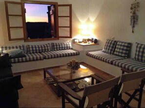 A living room with a sofa set, a coffee table, and a window with open shutters. - Doukaki’s House (Naxos)
