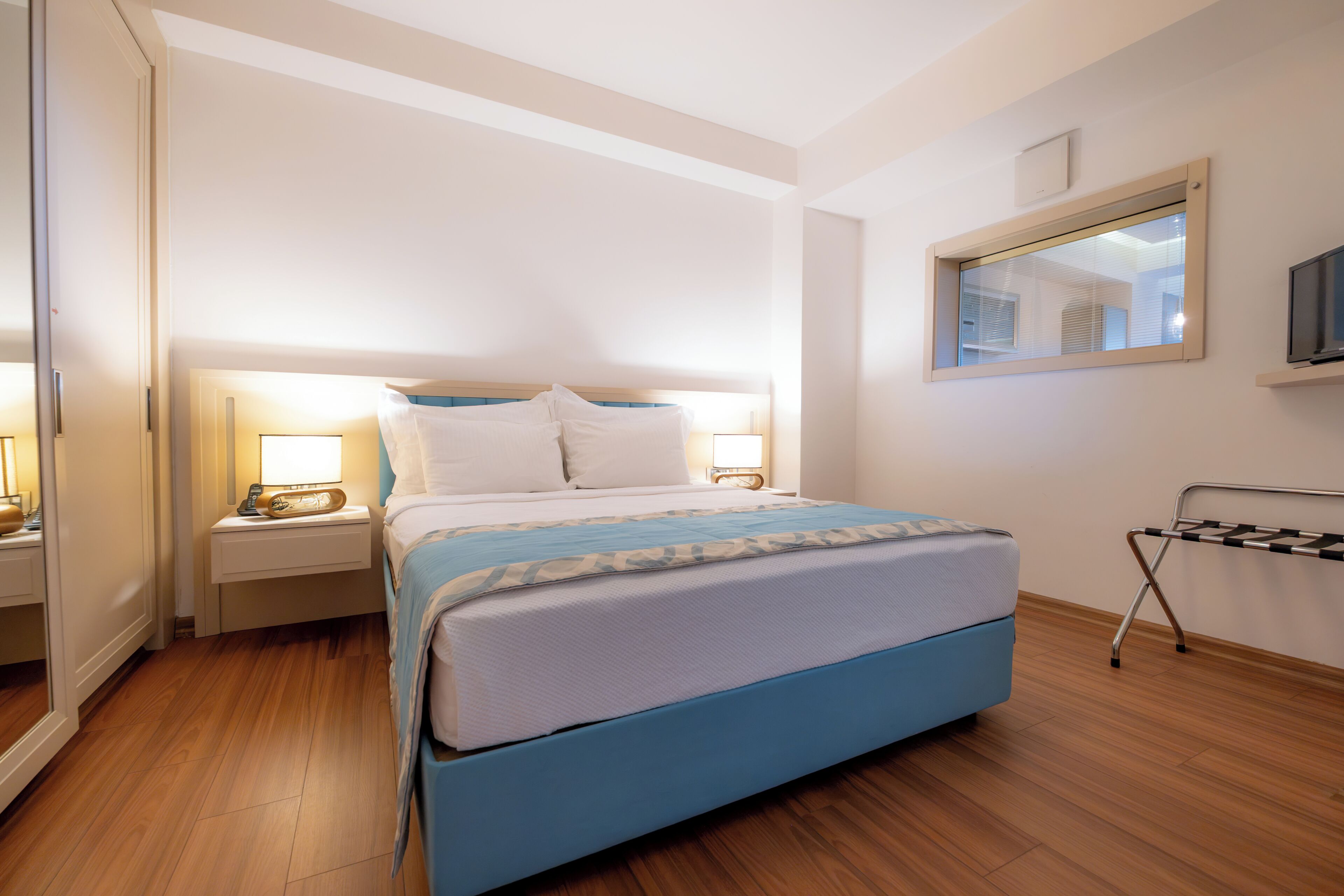 A hotel room with a bed, bedside lamps, a TV, and a window.