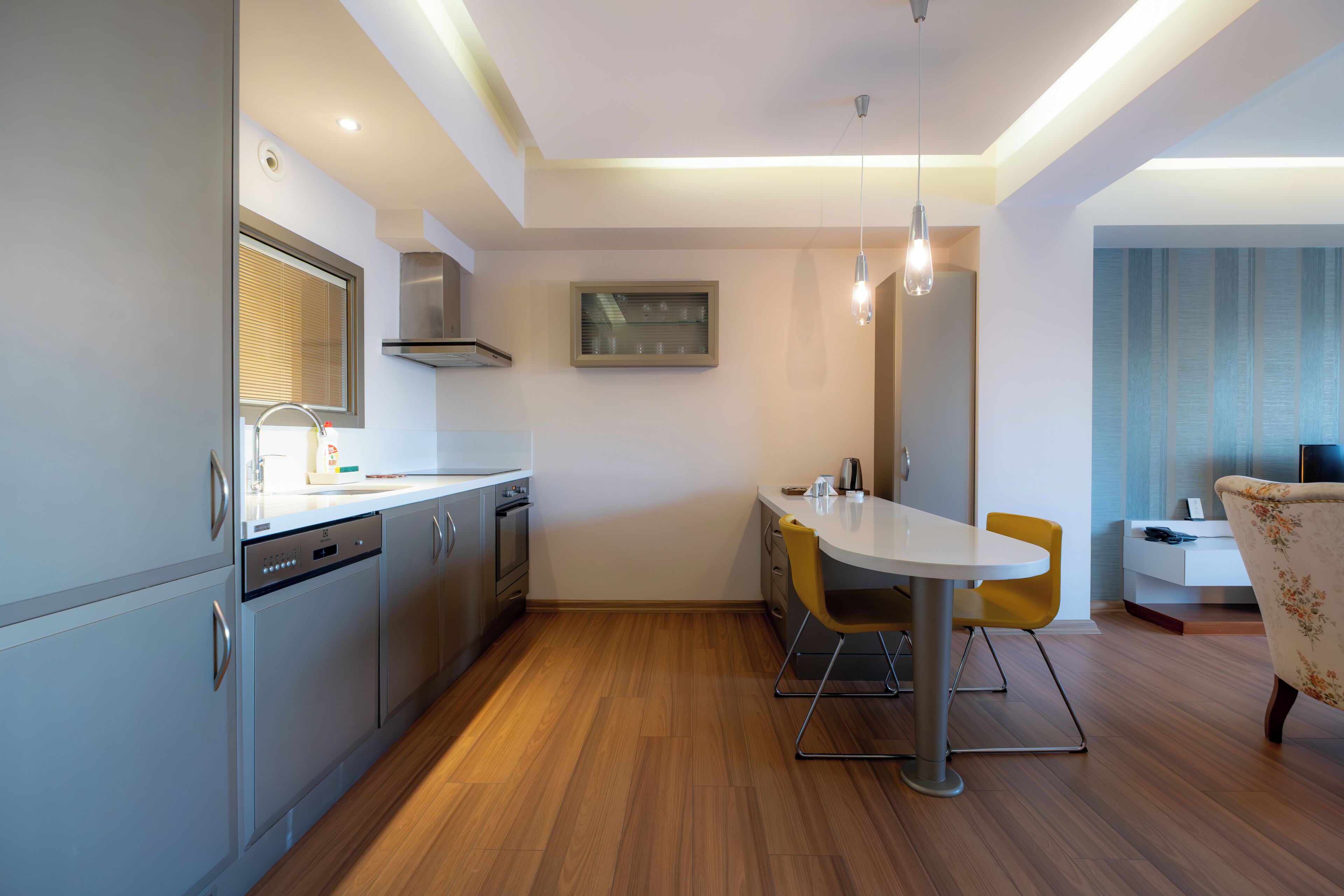 A modern kitchen with stainless steel appliances, a dining area with a white table and yellow chairs, and a small seating area with a sofa and a side table.