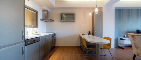 A modern kitchen with stainless steel appliances, a dining area with a white table and yellow chairs, and a small seating area with a sofa and a side table.