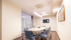 A conference room with a round table, six chairs, a flat-screen TV, and a painting on the wall. - Heykel Suites (Konak)