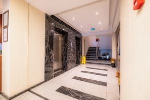 A hotel lobby with a marble floor, an elevator, and a staircase leading to another level.