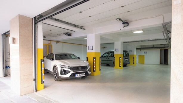A parking garage with two cars parked inside, one white and one gray. - Heykel Suites (Konak)