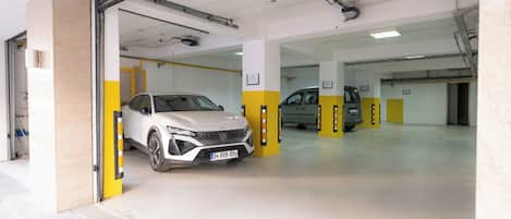 A parking garage with two cars parked inside, one white and one gray.