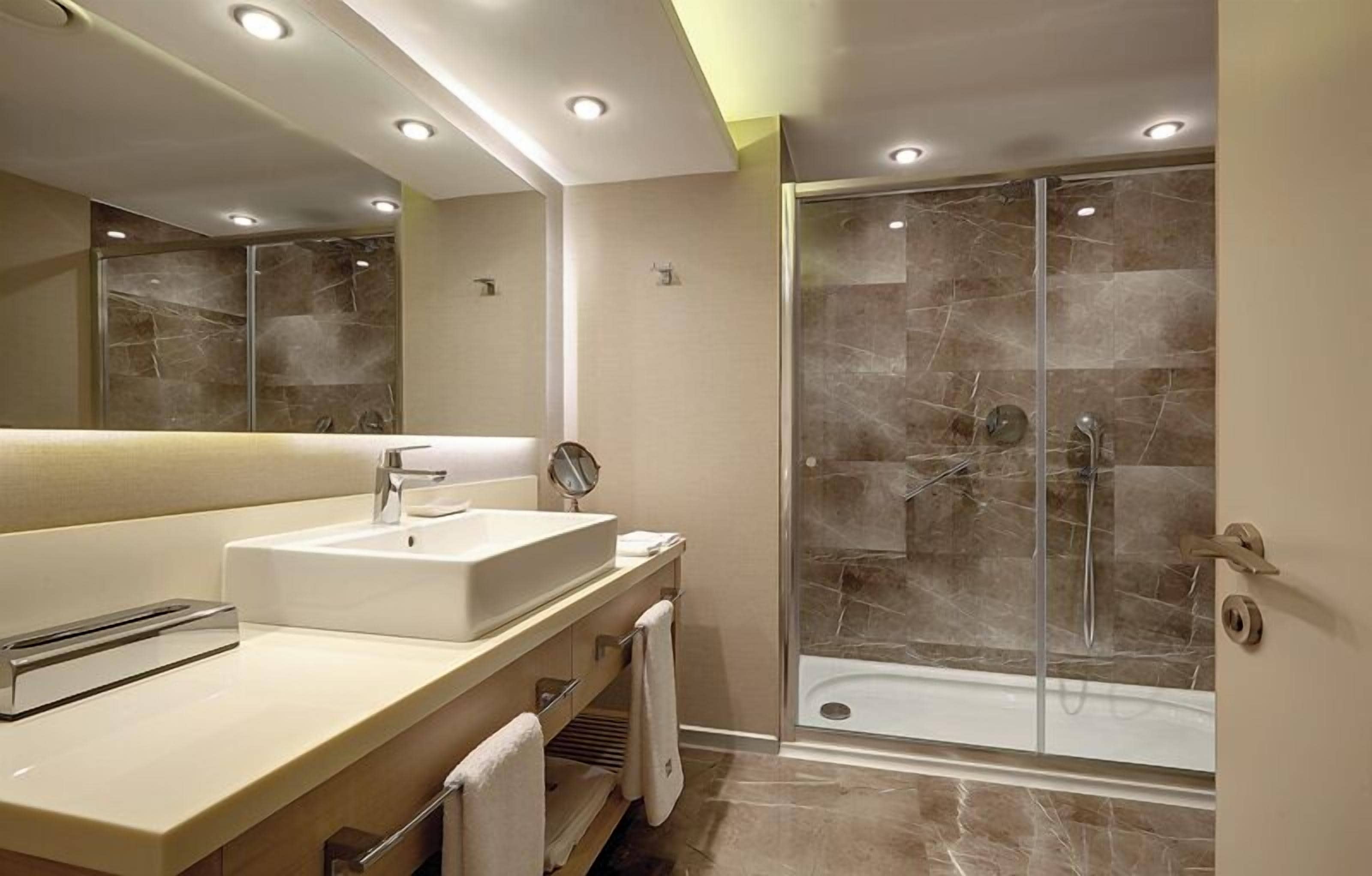 Un baño moderno con un espejo grande, un lavabo y una ducha con mampara de vidrio.