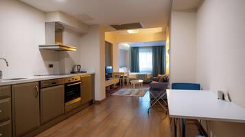 A modern kitchen with built-in appliances, a dining area with a table and chairs, and a living space with a sofa and a TV.