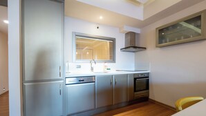 A compact kitchen with a built-in dishwasher, oven, and a window with blinds. - Heykel Suites (Konak)