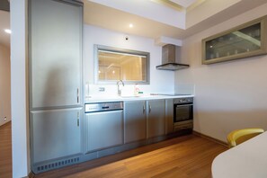 A compact kitchen with a built-in dishwasher, oven, and a window with blinds.