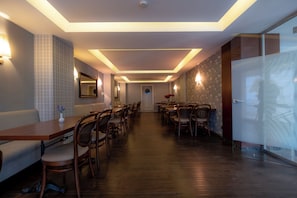 A hotel dining area with a long table, chairs, and a wall-mounted mirror.