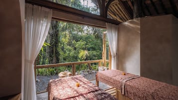 A room with two beds, a window with curtains, and a view of greenery outside.