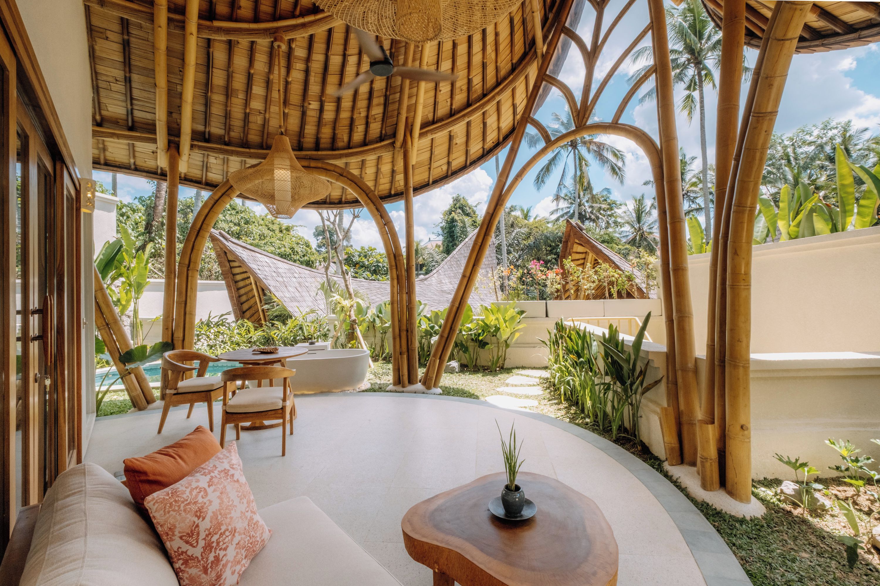 Un espacio al aire libre techado con una mesa de madera curva, techo tejido y vistas de vegetación tropical.