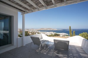 Une terrasse avec deux chaises et une table, d’où l’on peut admirer une ville c ôtière aux bâtiments blancs et un ciel d’un bleu limpide.