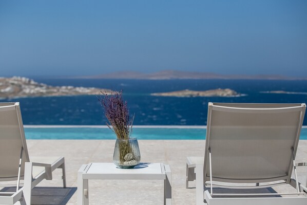 A view from a balcony overlooking a pool with two lounge chairs facing the sea. - Mykonos Seabreeze Town Villa (Mykonos)
