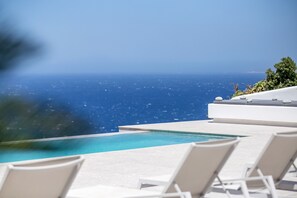 A pool with clear blue water, surrounded by white lounge chairs and a view of the ocean. - Mykonos Seabreeze Town Villa (Mykonos)