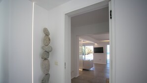 Un couloir orné d’une installation artistique murale en pierre, une porte donnant sur une pièce dotée d’une grande fenêtre et un aménagement intérieur moderne.