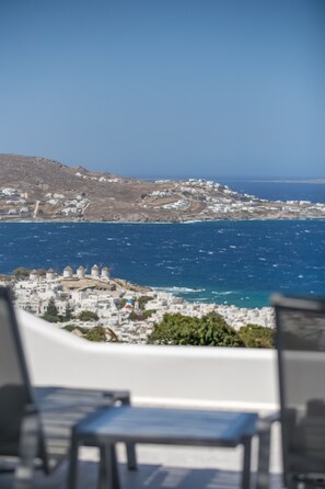 A coastal view with a chair in the foreground, a hillside with buildings, and the sea. - Mykonos Seabreeze Town Villa (Mykonos)