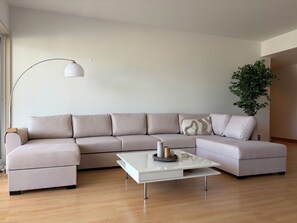 Ein modernes Wohnzimmer mit einer Eckcouch, einem Couchtisch, einer Stehlampe und einem Topfpflanzen.