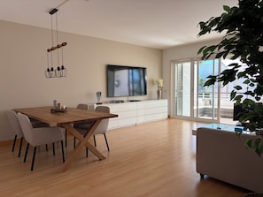 Ein modernes Wohnzimmer mit einem Holzespeisetisch, einem weißen Sofa und einem großen Fernseher an der Wand.