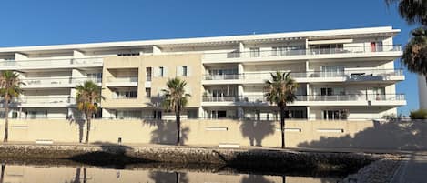 A multi-story hotel with balconies, palm trees, and a reflection in the water.