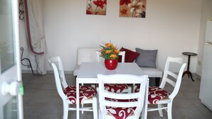 A dining area with a white table, red and white patterned chairs, a red vase with flowers, and a white sofa with red cushions.