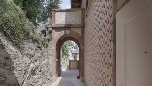 Un pasillo estrecho con una pared de piedra a un lado y una pared con diseño al otro, que lleva a una puerta.