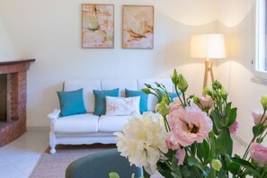 Ein Wohnzimmer mit einem weißen Sofa, türkisfarbenen Kissen, einem Kamin und einer Lampe.